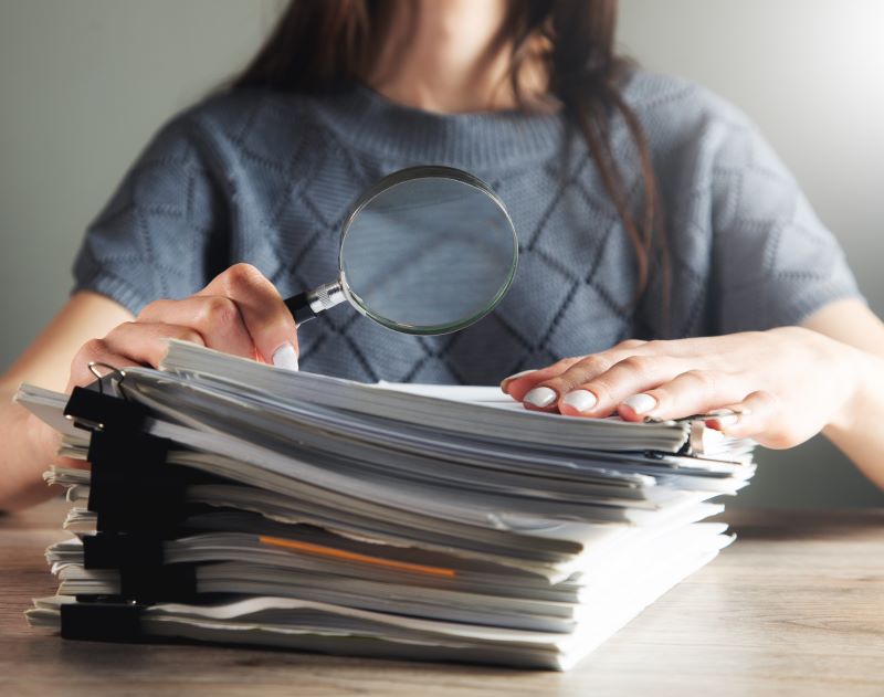 Women holding a magnifying glass close to a stack of documents